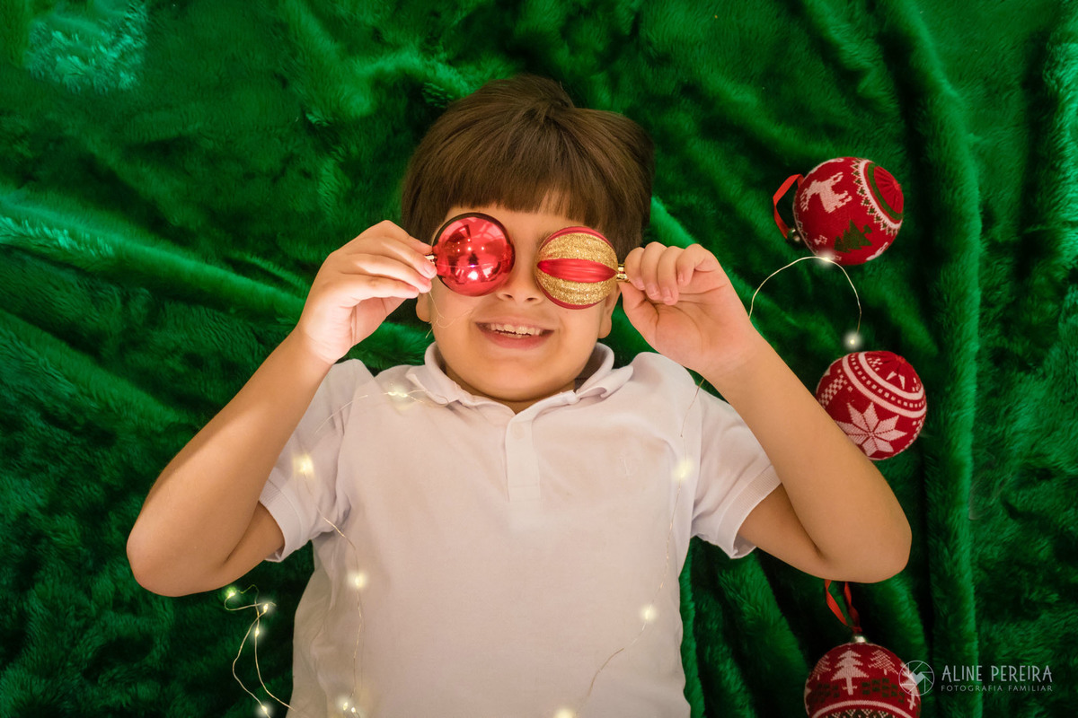menino sentando no tapete verde com bolas de natal no lugar dos olhos