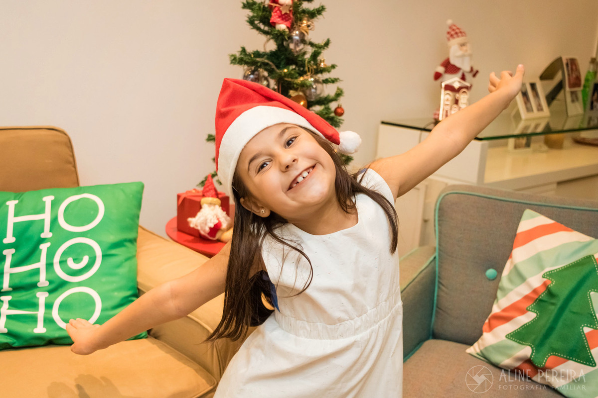 menina de bracos abertos em frente a árvore de natal