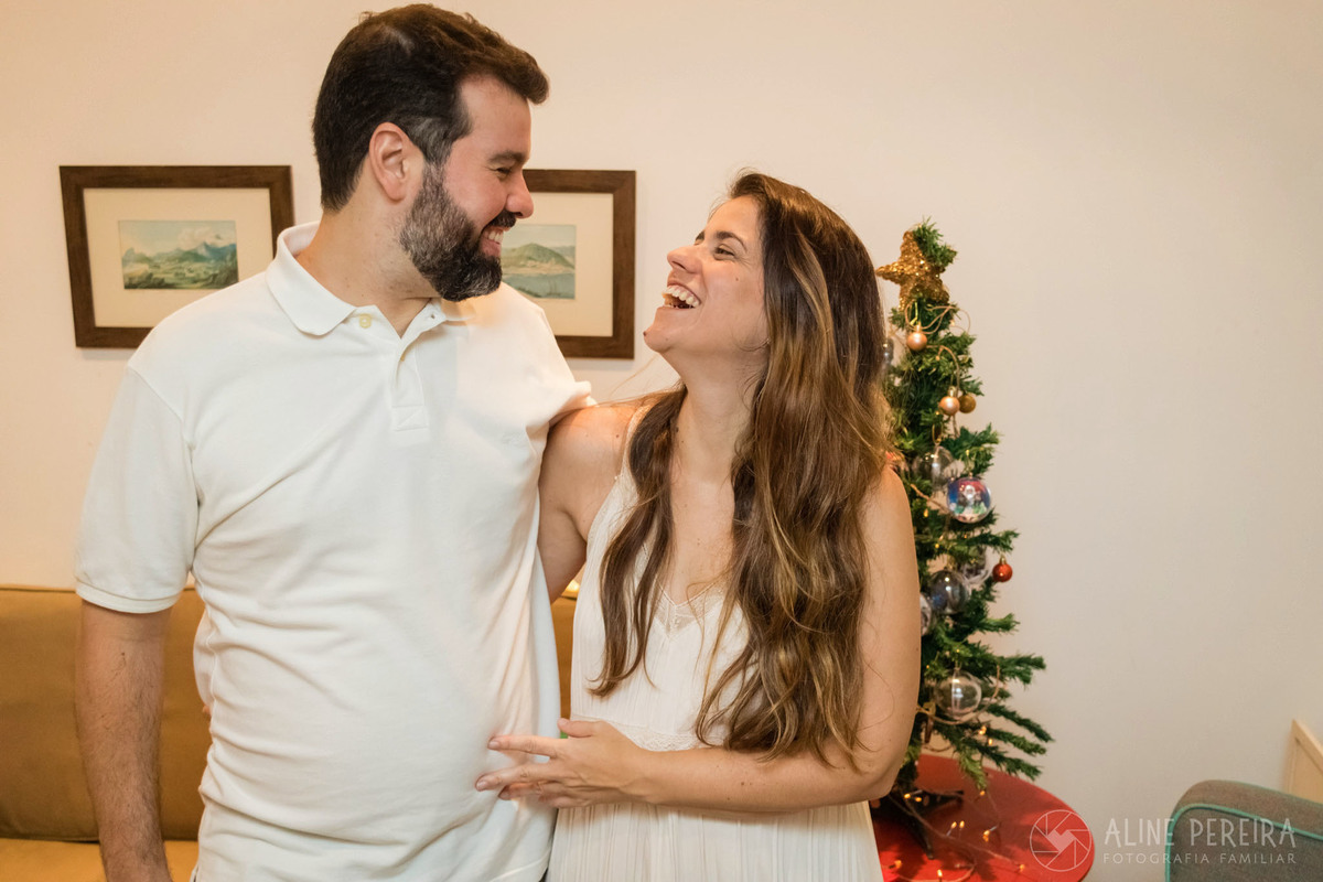 casal se olhando e sorrindo com a árvore de natal ao fundo