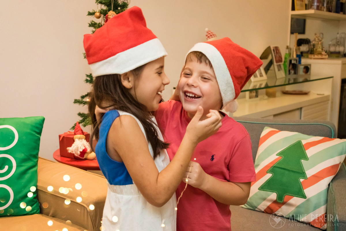 crianças com chapeuzinho de papai noel em frente a árvore de natal