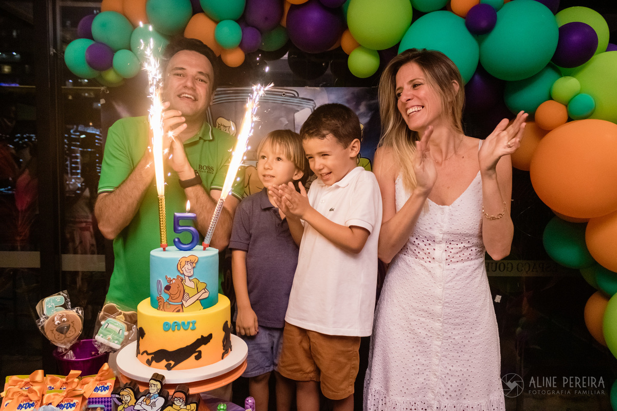 aniversariante cantando parabéns com a familia na mesa do bolo decorada com o tema scooby-doo