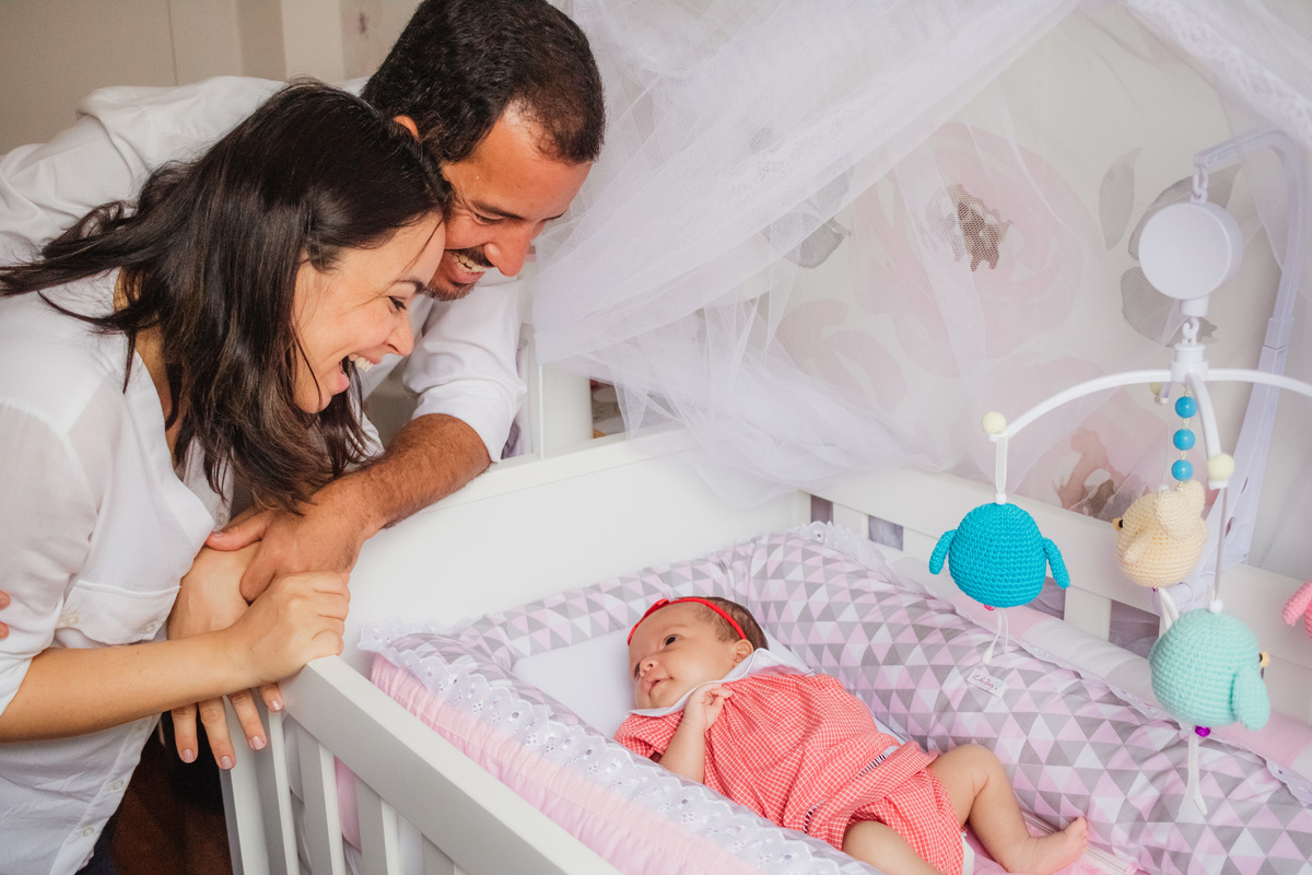 pais apoiados no berço, olhando para a filha