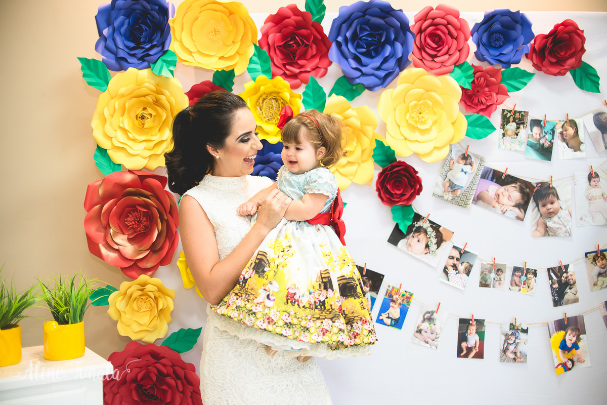 mãe e filha brincando na festa de 1 ano na frente de flores de papel e varal de fotos