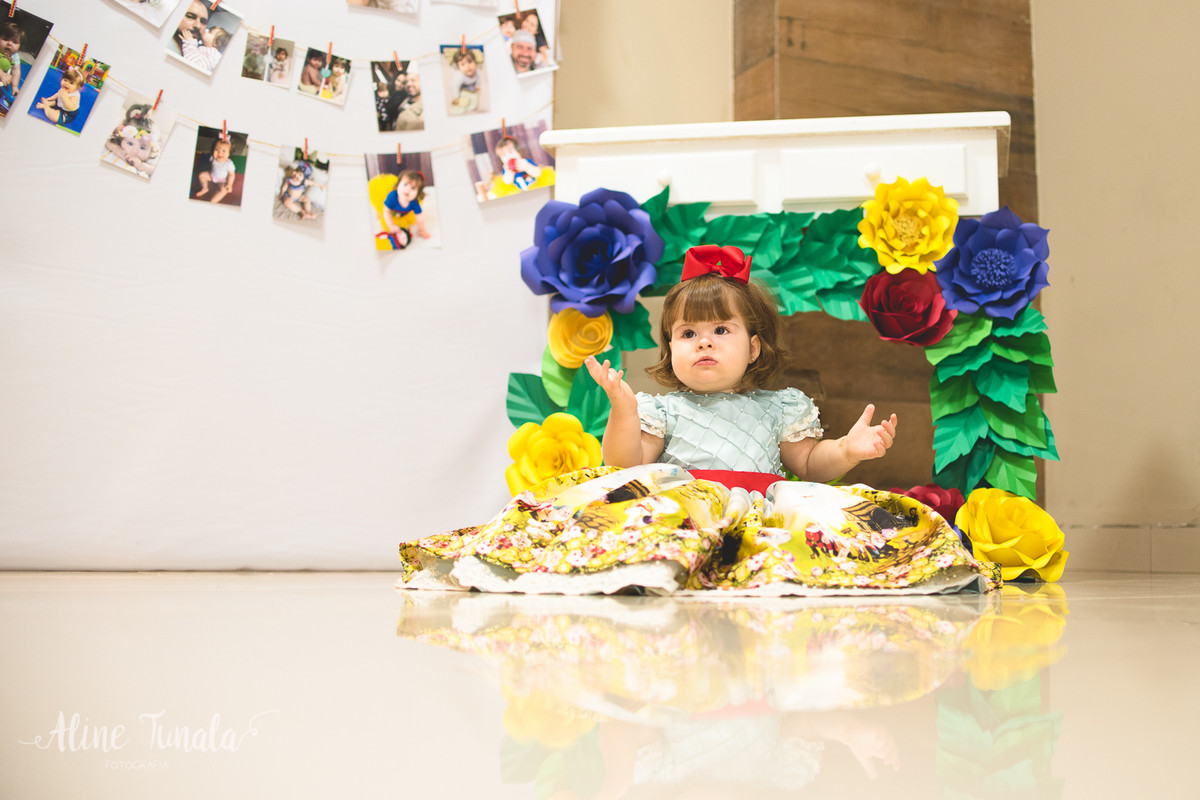 bebê na sua festa de 1 ano de branca de nece com decoração de flores de papel e varal de fotos