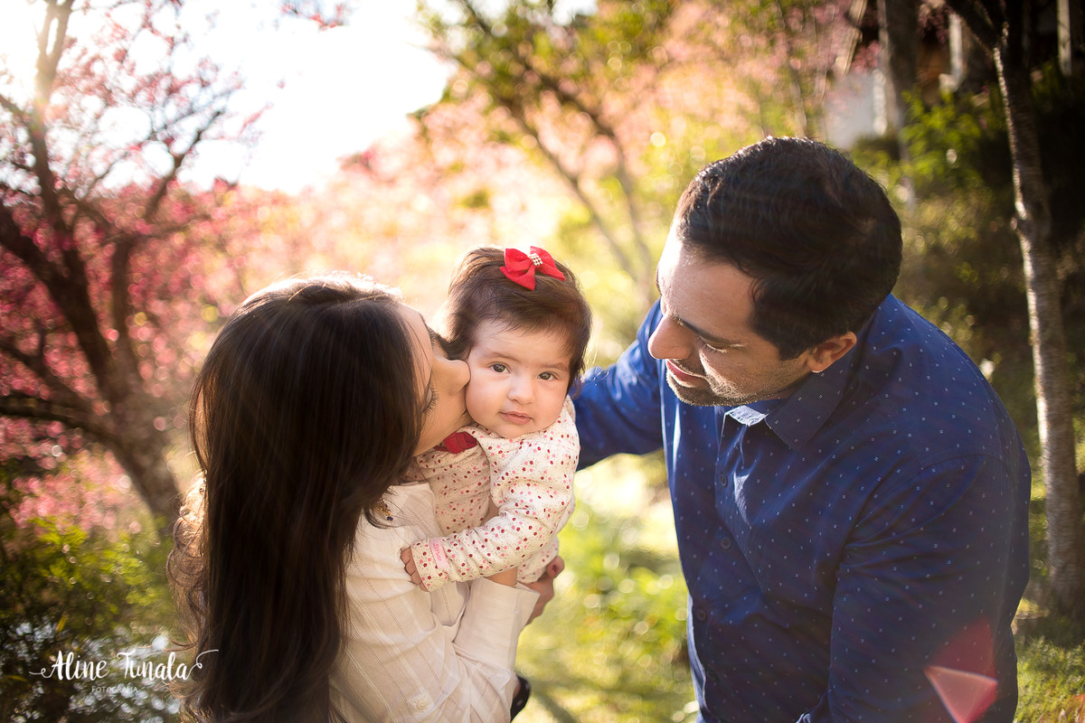 mamãe beijando bebê no ensaio de acompanhamento de 4 meses no fim de tarde com cerejeiras abertas