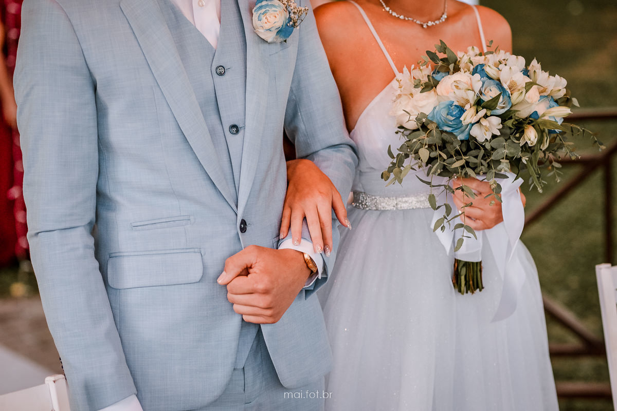 detalhe das mãos da noiva e do noivo e buque de flores durante a cerimonia de casamento 