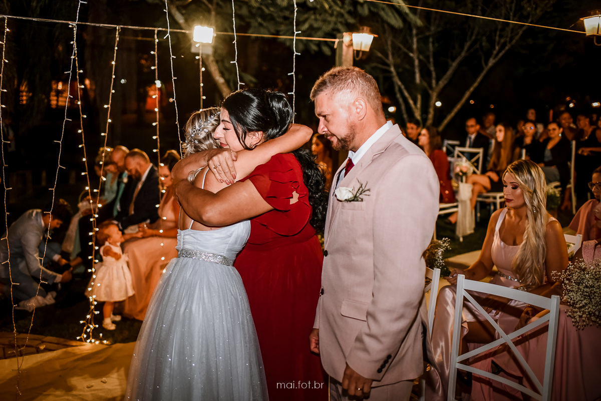 noiva abraça mãe após lavar seus pés, ao fundo noivo lavando os pés de sua mãe  