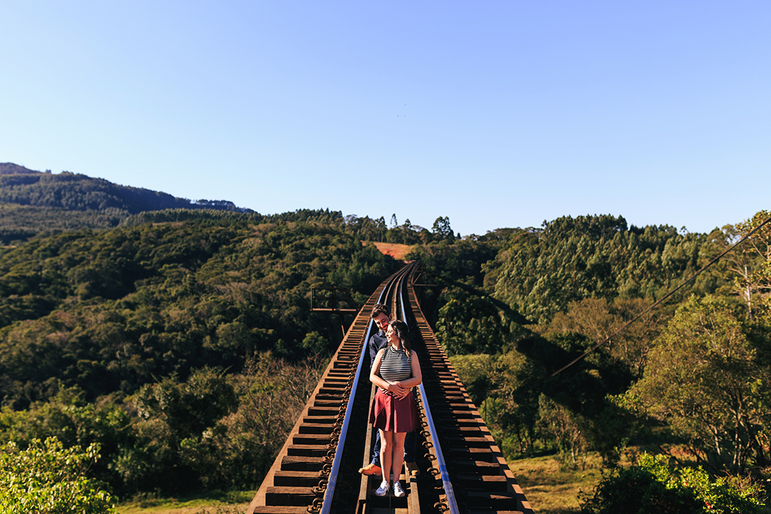 noivos em cima de ponte se abracados com o rosto virado para o sol