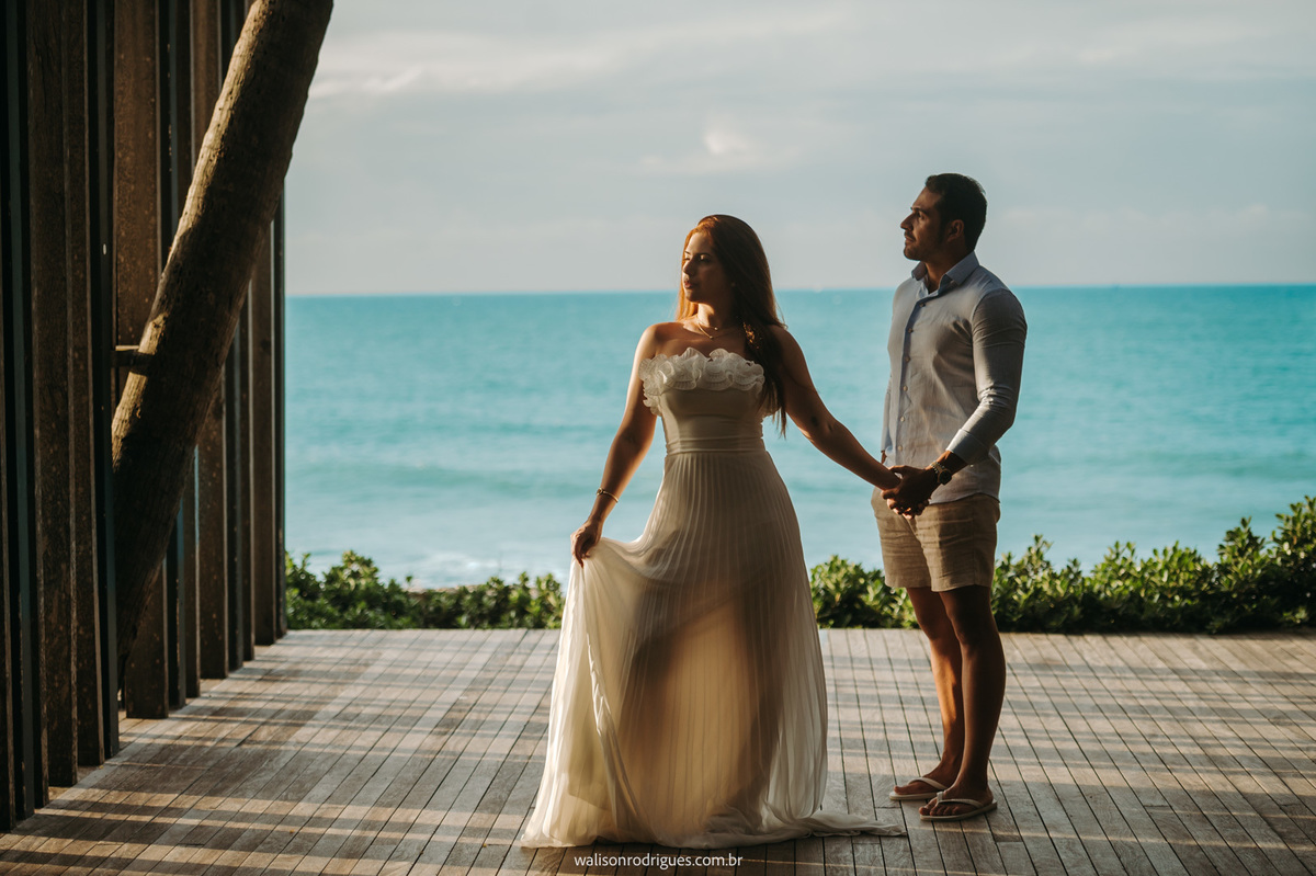 Casal sorrindo à beira-mar durante sessão de fotos pré casamento.