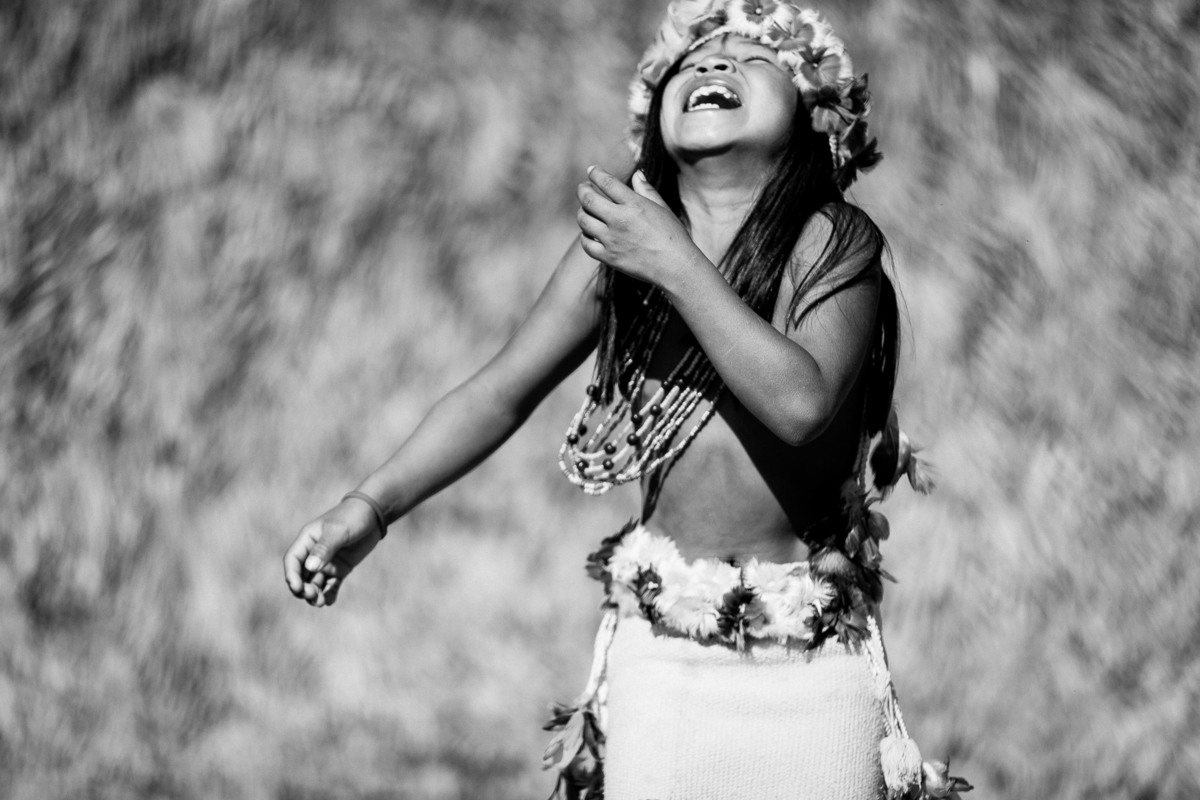 menina índia sorrindo para o alto com colar e arco de flores na área indígena do oeste do mato grosso na aldeia parecis,  fotografia por alê carnieri