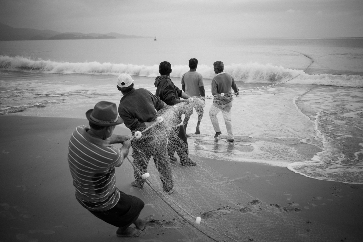 cinco homens puxando rede na praia na pesca da tainha em Florianópolis - SC, fotografia por Alê Carnieri
