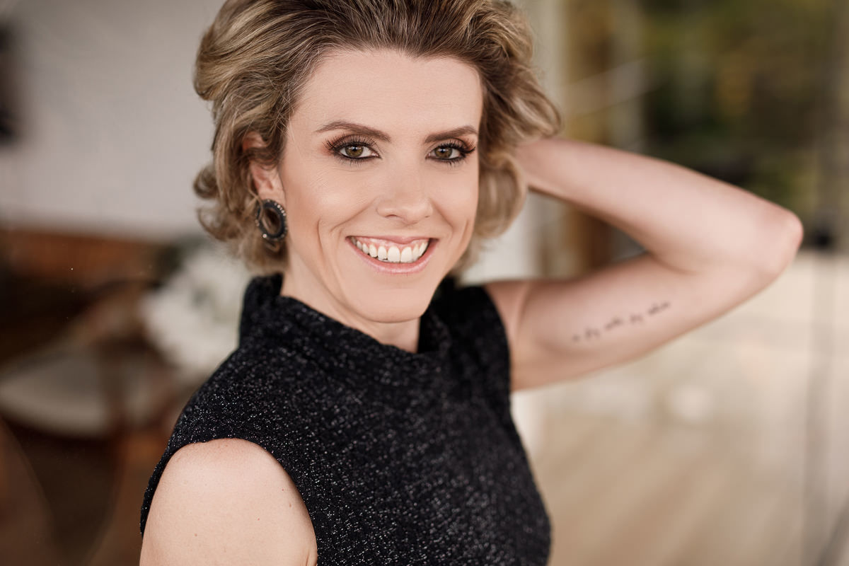 Modelo Ana Paula olhando para camera e sorrindo, mostrando tatuagem no braço esquerdo