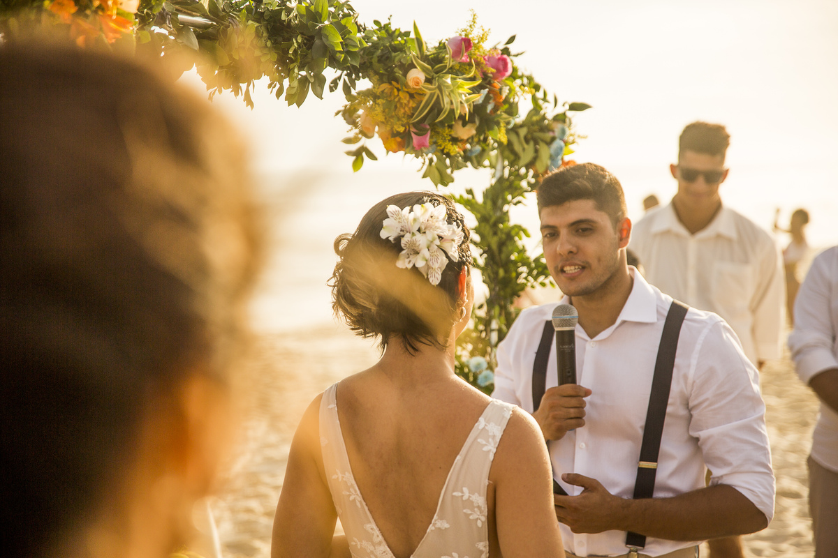 noivo com blusa branca e suspensório lendo os votos para a noiva em casamento na praia