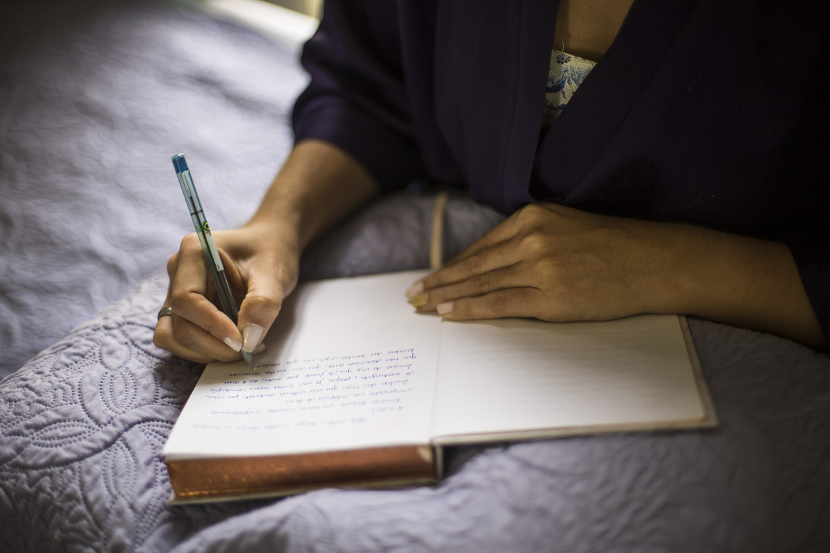 caderno aberto com as mãos de uma noiva escrevendo os seus votos durante o making of.