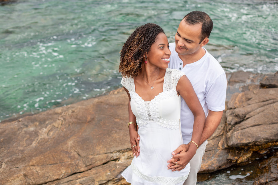 Noivos abraçados, o noivo com as mãos na cintura da noiva, em uma foto de ensaio pré-wedding com iluminação natural em Búzios, Rio de Janeiro.
