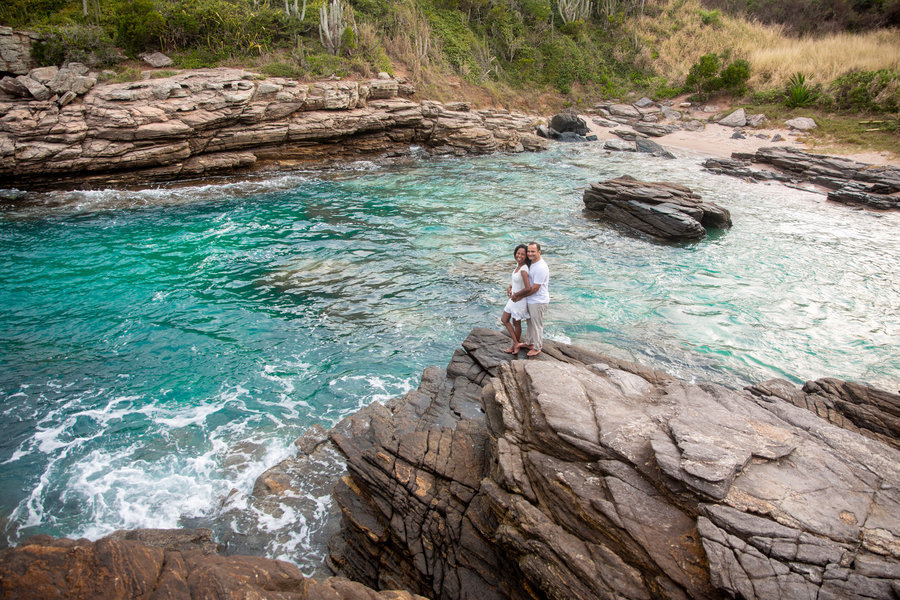 imagem vista de cima com uma grande angular com os noivos em cima de uma pedra. Eles estão centralizados na imagem. Ao fundo se vê as águas verdes cristalinas da praia de búzios.
