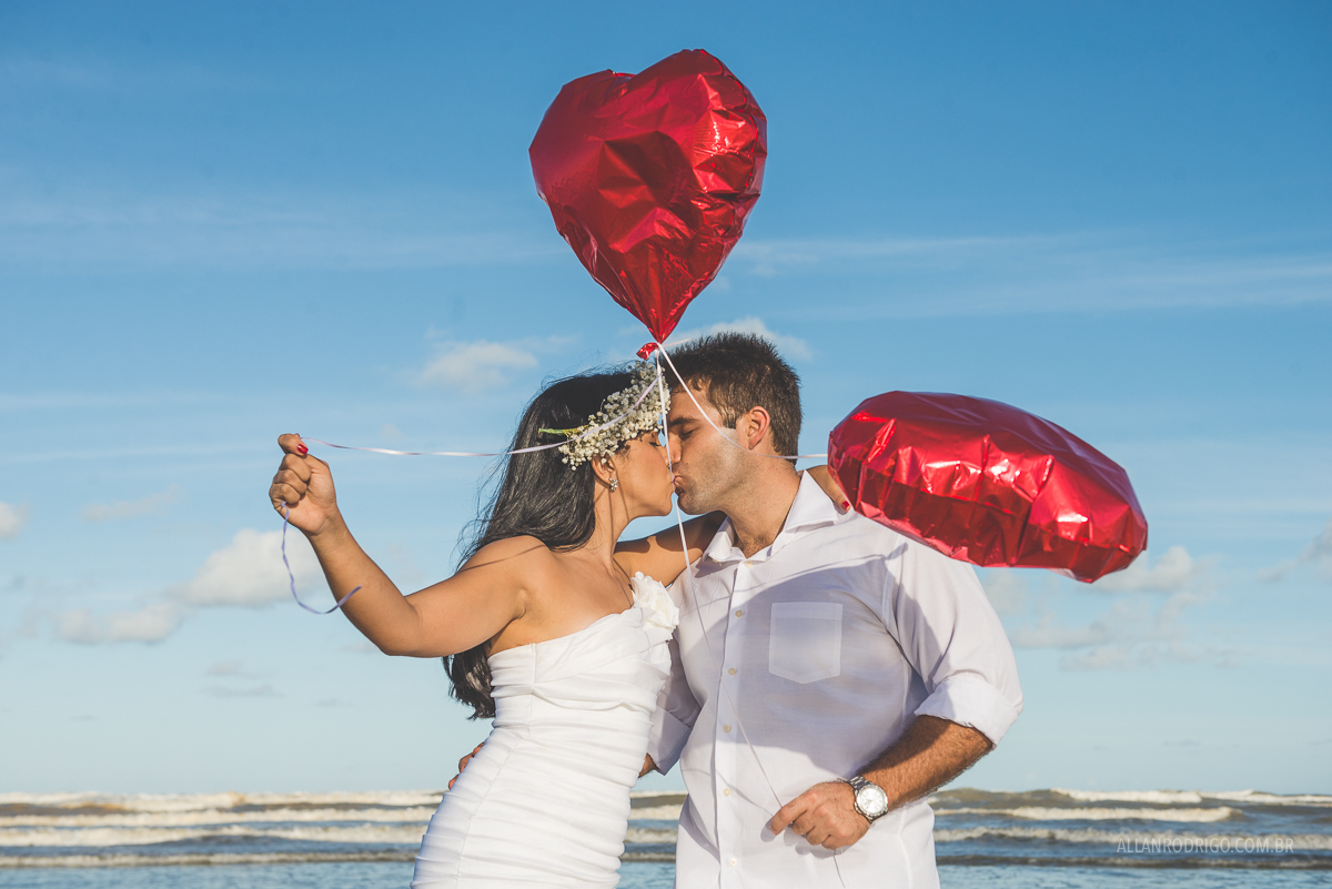 casal se beijando na praia com baloes de coração