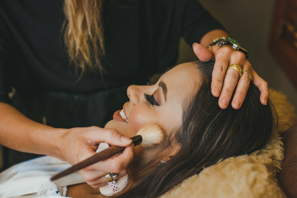 Noiva feliz, sorrindo, sendo maquiada por Josiane Arruda
