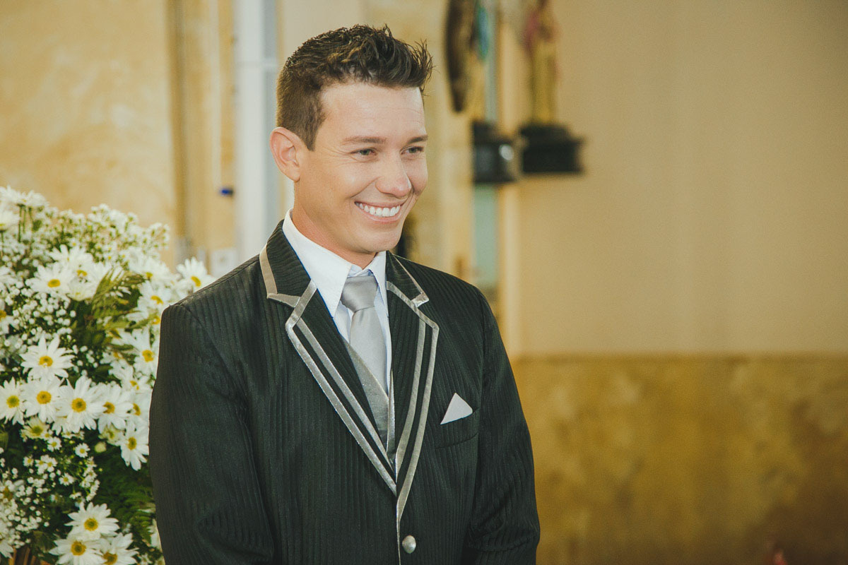 Noivo sorri ao ver a noiva entrando pela porta da igreja.