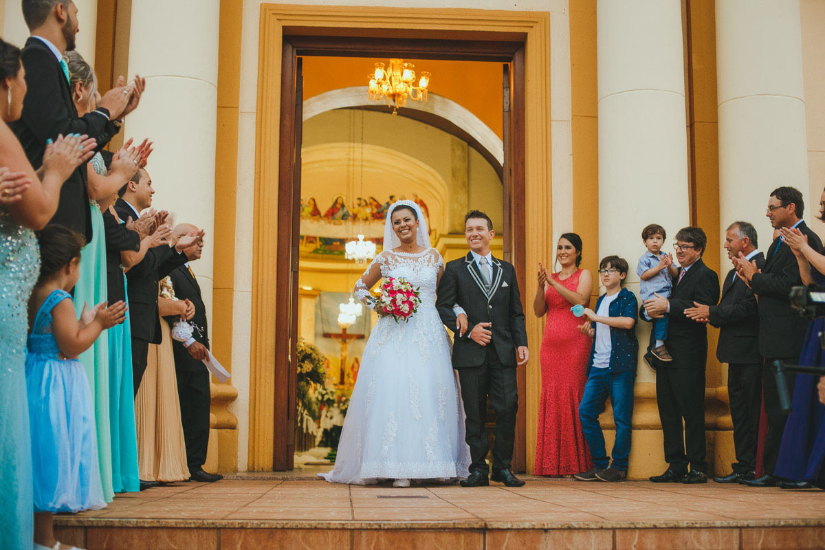 Com os padrinhos alinhados na porta da igreja o casal sai e é recibo por palmas.