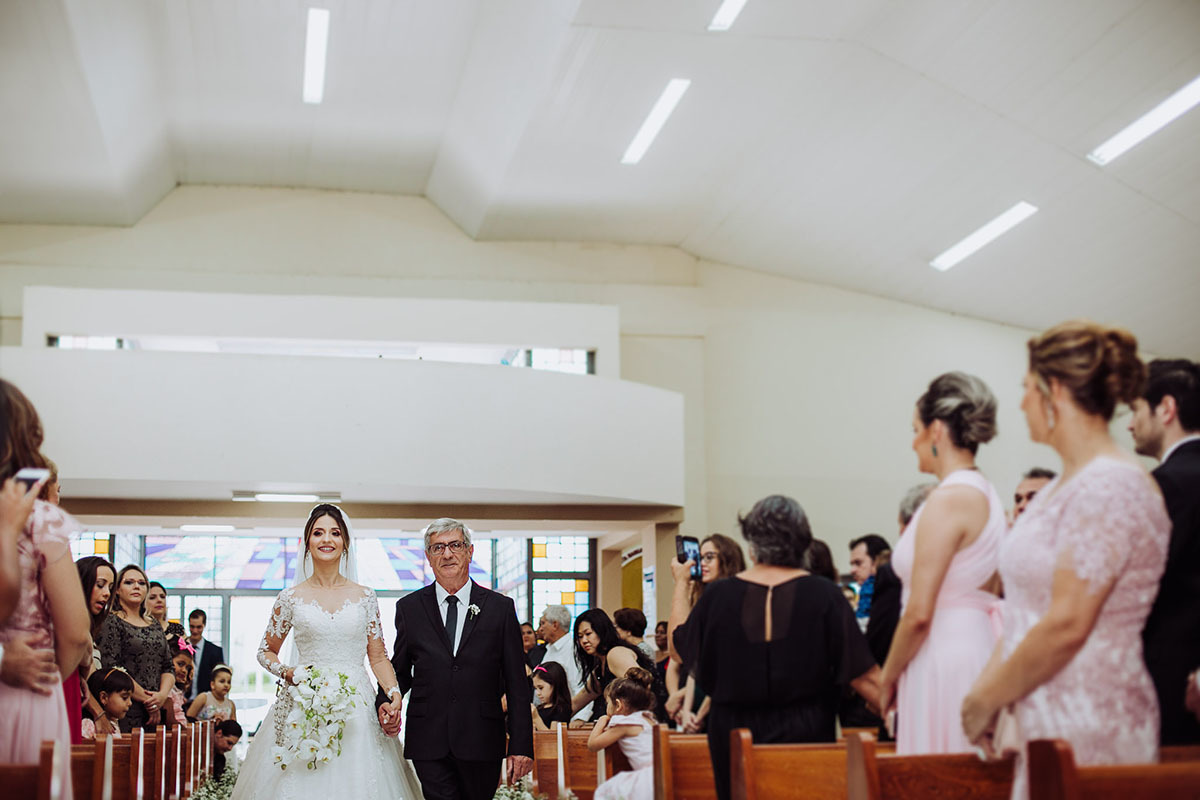 Enfim a entrada da noiva, com seu pai, os convidados em pé assistem ao cortejo.