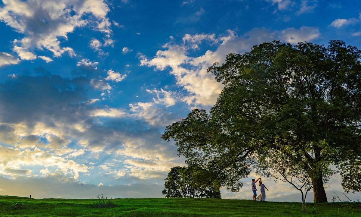 a composição de uma bela fotografia de pré wedding do casal Isabelle e Diego dançando em baixo de uma arvore ao fundo lindas nuvens e um céu azul (fotografia André Monteiro)