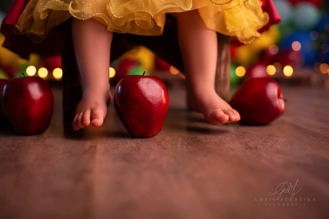 Smash the cake branca de neve ensaio de bebe branca de neve mostrando apenas os pes que estao sentados em uma cadeira e macas ao chao