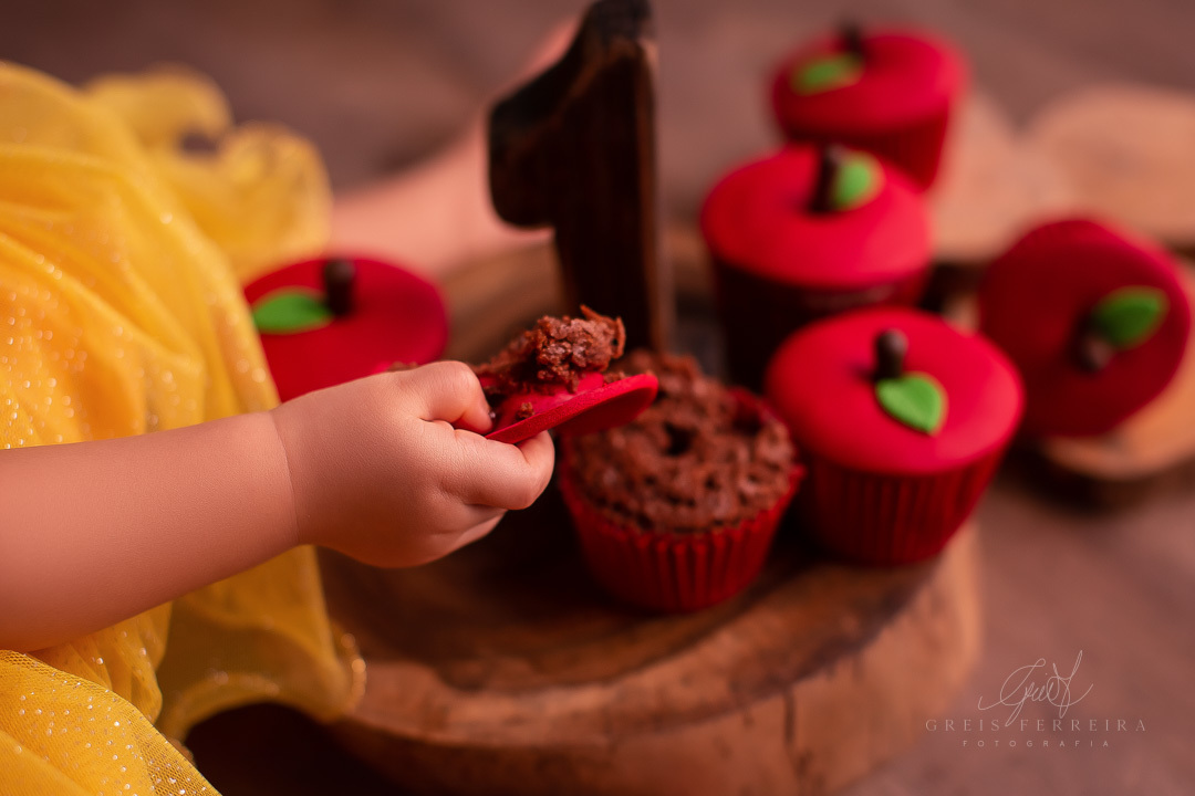 smash the cake branca de neve cupcake formato de maca sobre fatia de madeira e numeral 1 uma mao pegando um cupcake destruido