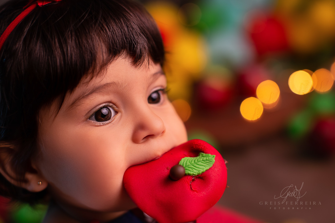 retrato de rosto bebe de 1 ano olhando para a direita com uma maca de biscuit na boca e fundo com bokeh
