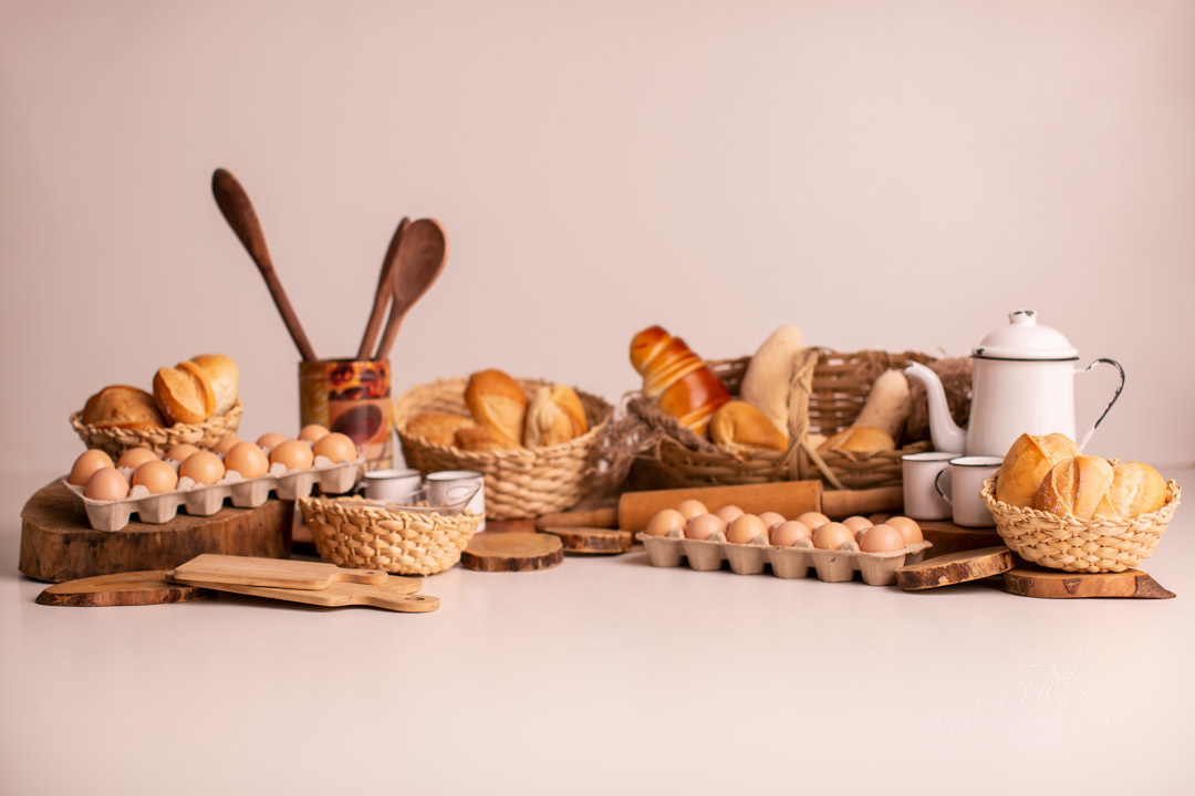 ensaio de bebe 9 meses padeiro com paes em cestos colheres de pau bule de cafe ovos e rolo de massa de madeira