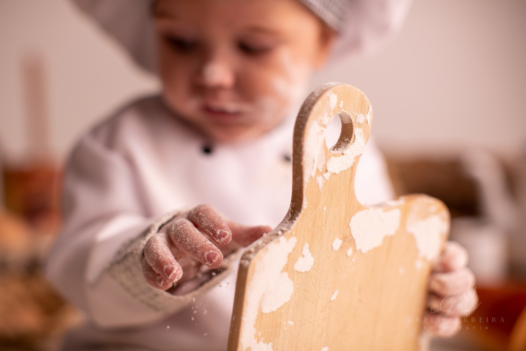 ensaio de bebe de 9 meses de padaria segurando uma tabua de madeira suja de farinha