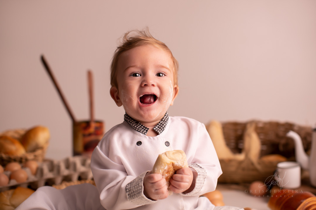 ensaio de bebe sujo de farinha de 9 meses de padaria segurando um pao e rindo