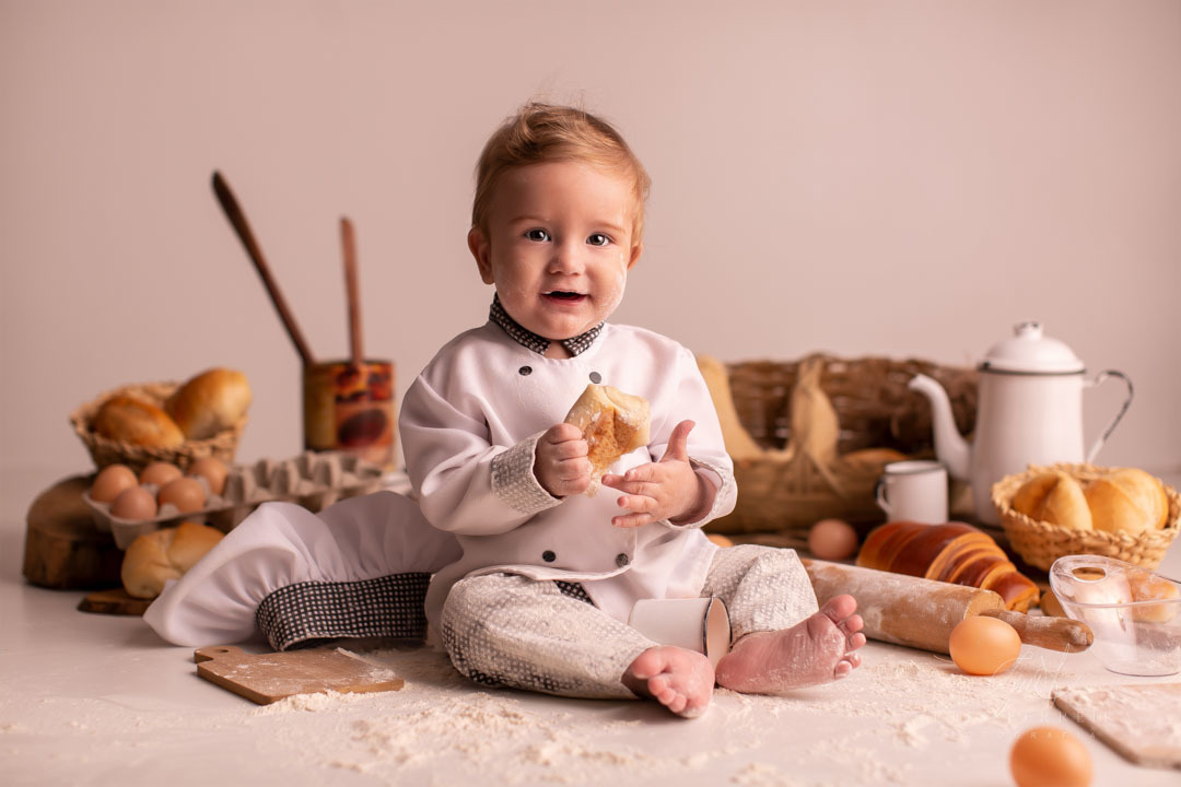 ensaio de bebe sujo de farinha de 9 meses de padaria segurando um pao e olhando par afrente
