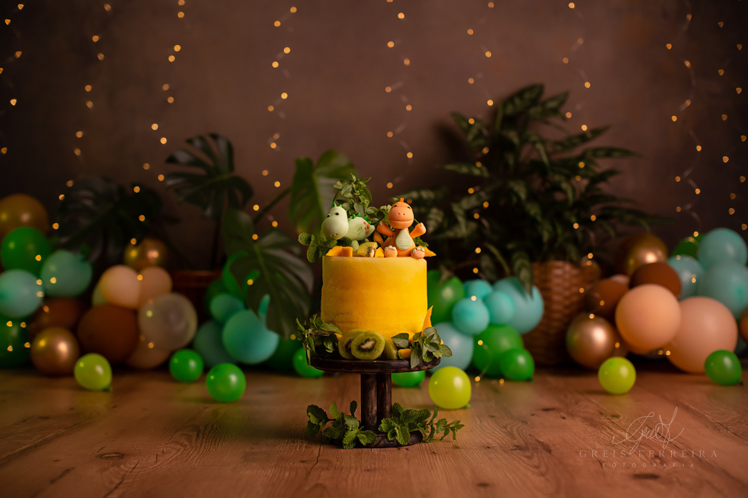 smash the fruit de dinossauro com um bolo de melancia amarela decorado com kiwi hortela manga  2 dinossauros de biscuit em um lindo pedestal de madeira ao fundo temos baloes plantas naturais e pisca-pisca