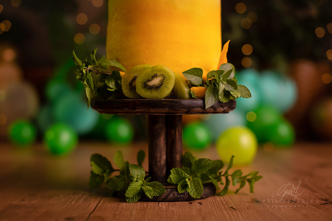 smash the fruit de dinossauro com um bolo de melancia amarela decorado com kiwi hortela manga  2 dinossauros de biscuit em um lindo pedestal de madeira ao fundo temos baloes plantas naturais e pisca-pisca