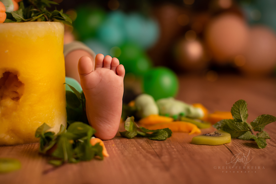 pe de bebe ao lado de um bolo destruido de melancia amarela decorado com kiwi hortela manga