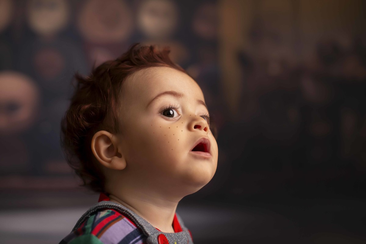 Chucky Boneco assassino bebe ruivo sentado em frente a uma estante de bonecos macabros