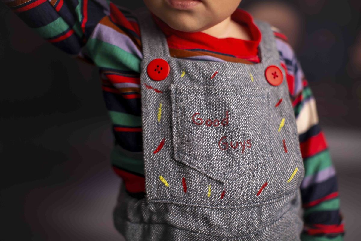 Chucky Boneco assassino bebe ruivo sentado em frente a uma estante de bonecos macabros