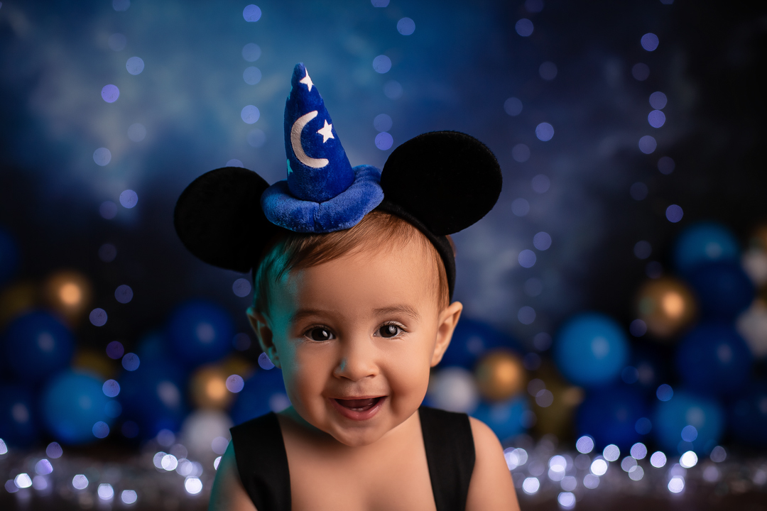 Smash the cake mickey ensaio de bebe chapeu de feiticeiro com orelhas do mickey nacabeça de um bebe sorrindo com fundo azul piscas e baloes desfocado