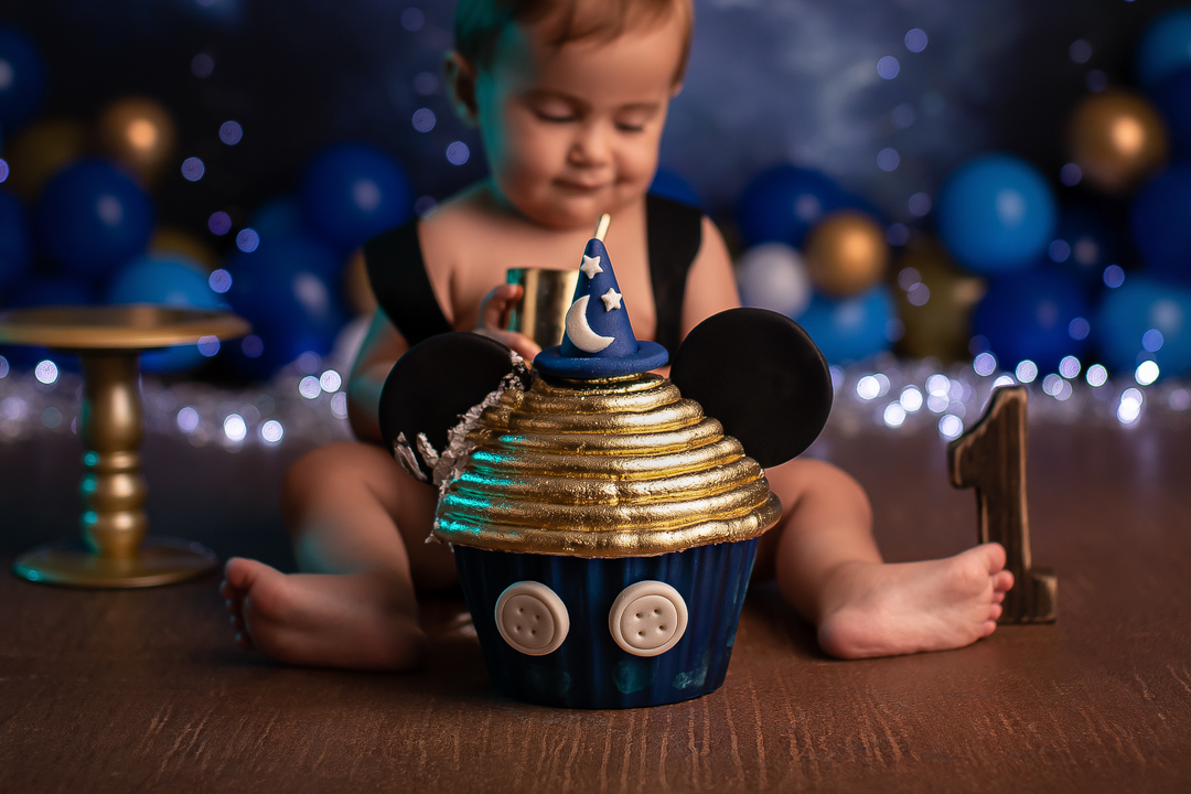 Smash the cake mickey ensaio de bebe com bolo de chapeu de feiticeiro com orelhas do mickeycom bebe sentado no chao sorrindo com  com fundo azul piscas e baloes desfocado