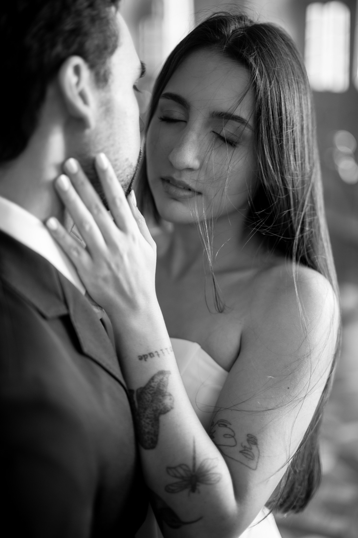 Fotografia a preto e branco a destacar o carinho das mãos no rosto e pescoço. Detalhe íntimo do casal durante sessão fotográfica de casamento de luxo