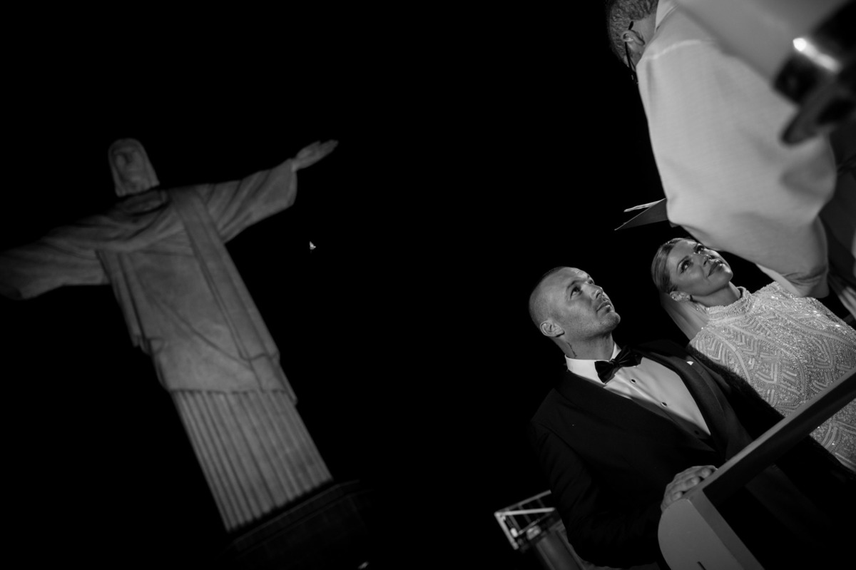 casal de noivos recebe benção de padre aos pes do cristo redentor em cerimonia de casamento