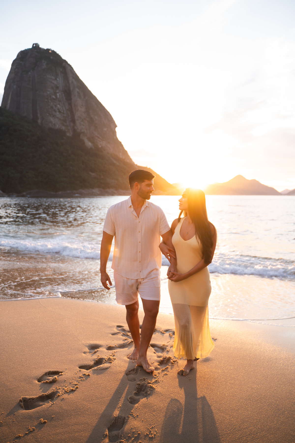 casal de noivos caminha se olhando em praia do rio de janeiro ao nascer do sol 