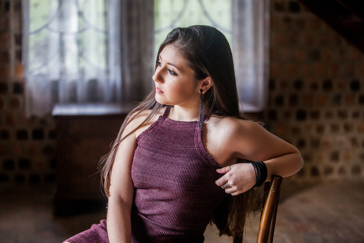 jovem de vestido na cor vinho sentada em cadeira de madeira