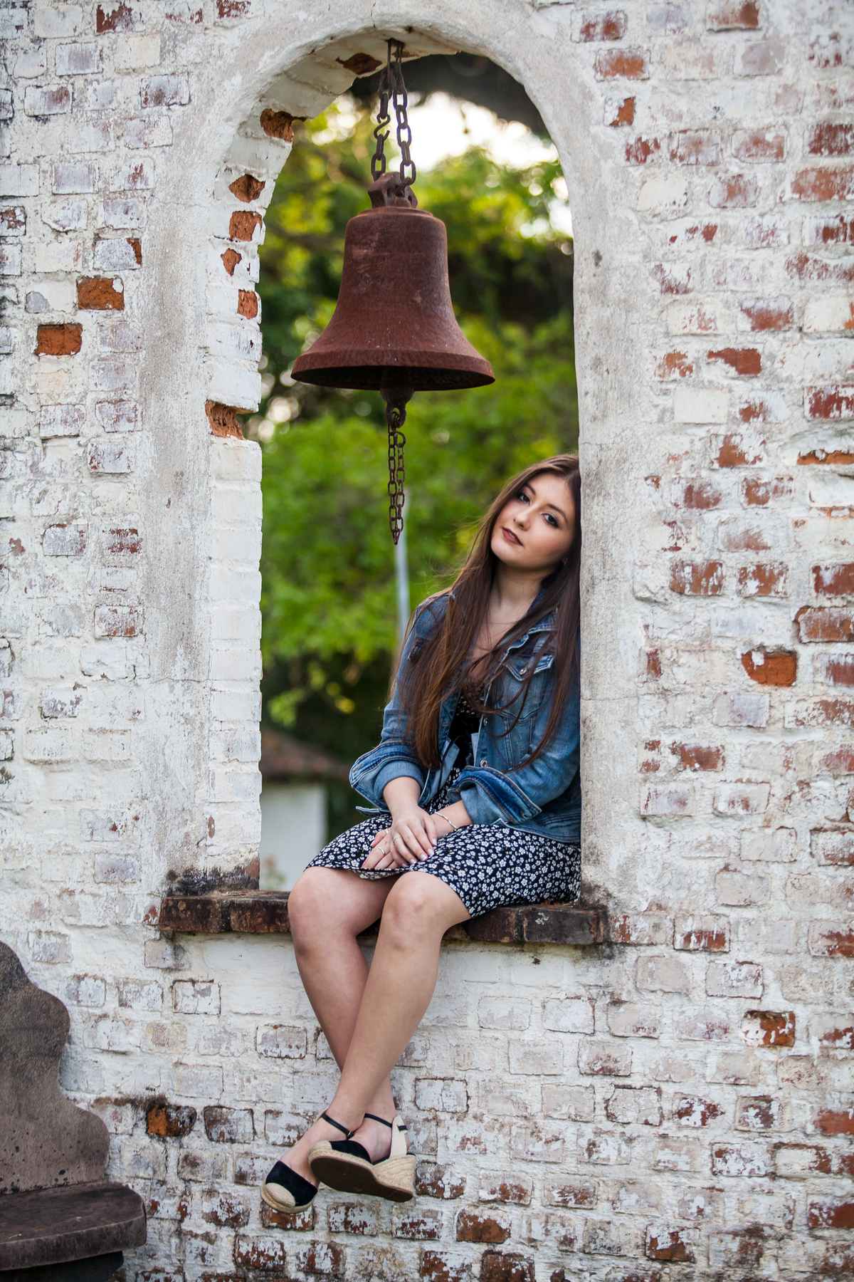 jovem de vestidinho floral e jaqueta jeans sentada em arco de pedra