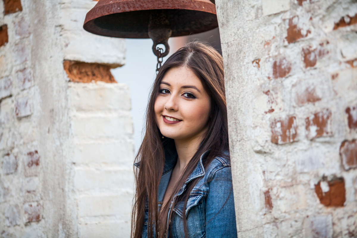 foto close de jovem de vestidinho floral e jaqueta jeans sentada em arco de pedra