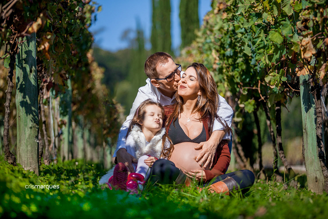 gestante e família sentados no chão em meio a vinhas