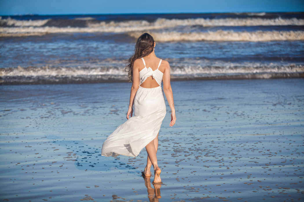 jovem de vestido branco caminhando em direção ao mar