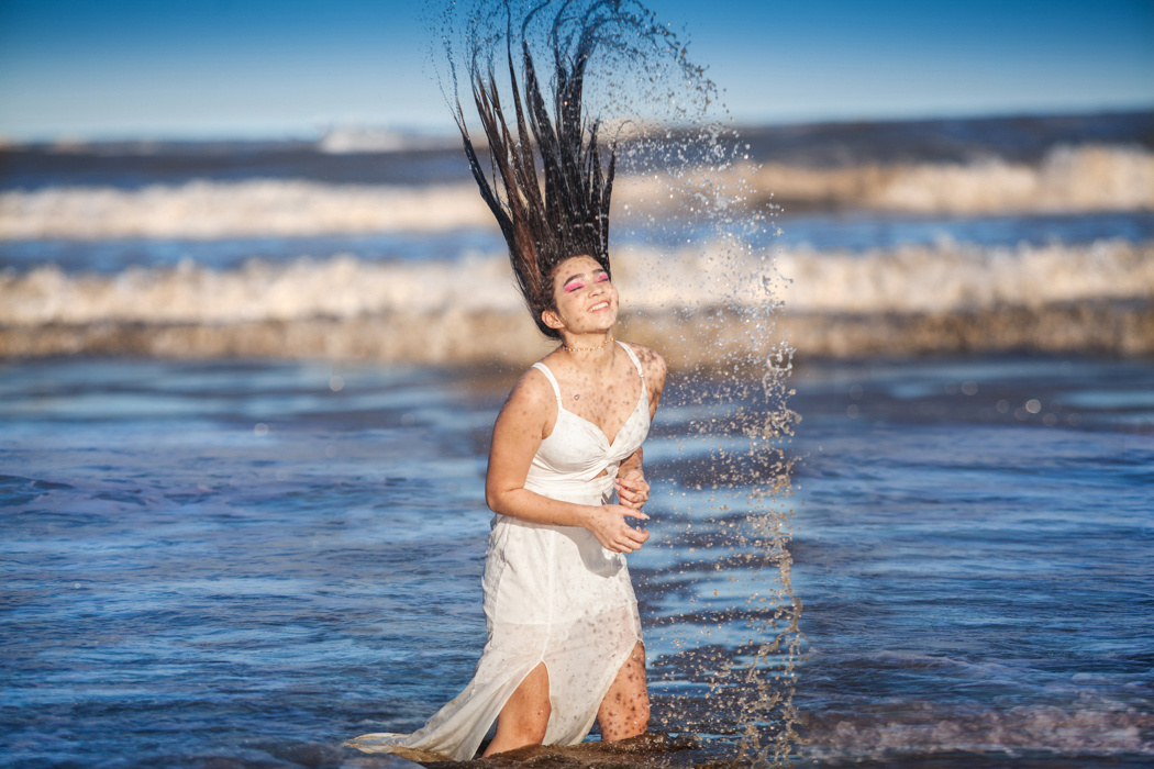 jovem mergulha cabelo na água do mar e joga cabeça para trás espalhando os pingos