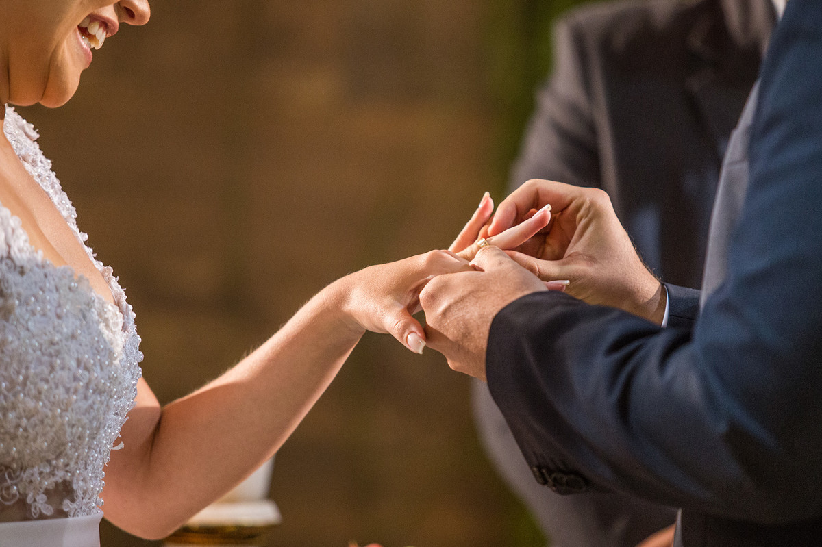 Detalhe do noivo colocando a aliança na mão da noiva na cerimônia do casamento